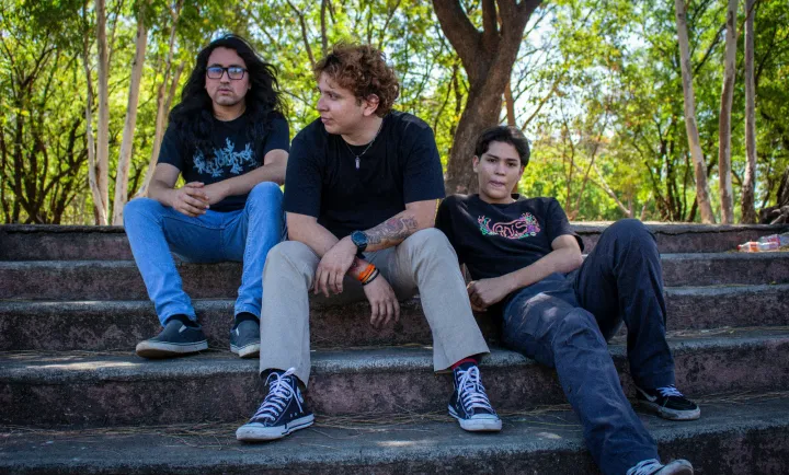 Three teenage boys sitting together on outdoor concrete steps, one turned toward the others mid-conversation.